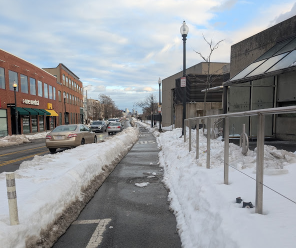 A snow-lined bike lane in Porter Square, with parked cars on the left side.