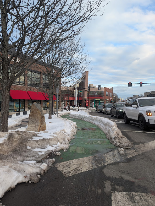 A thick mound of unplowed snow sits between the bike lane and the car lane on a street in Porter Square.